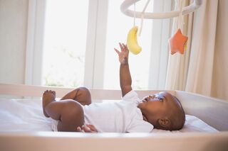 Adorable afro american baby boy lying in his crib playing with mobile